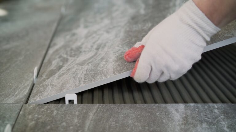 A worker puts a large tile on the floor.